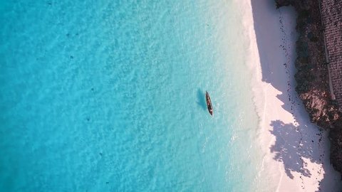 Aerial view of a poor fisherman with a torn shirt sails on a small boat on clear blue water along a tropical beach with beautiful hotels in Africa. Indian Ocean. Zanzibar. 2017