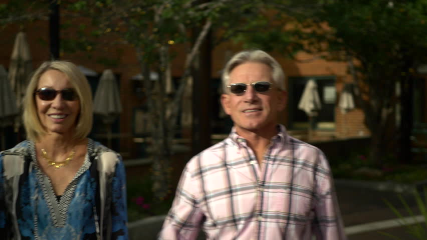 Attractive senior caucasian couple walk and laugh on historic Main Street, Park City, Utah at dusk.
