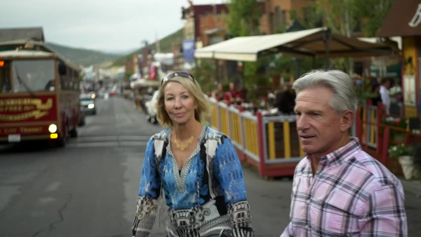 Attractive senior caucasian couple walk on historic Main Street with trolley in background, Park City, Utah at dusk.
