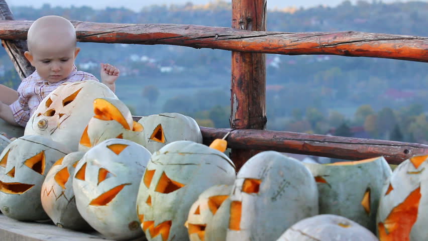 Cute baby face looking from behind a lot of scary Halloween yellow melons