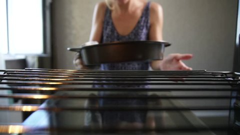 Closeup view of woman's hands taking out a baking pan from the oven. Homemade bakery