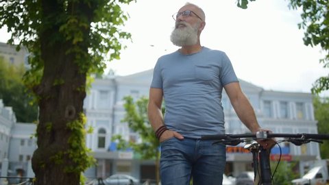 Amazed greyhaired man with bicycle examining city during walk