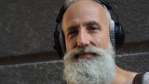 Serene greyhaired guy putting off his headphones outdoors