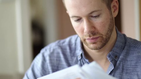 A man in debt is worried and stressed whilst looking through bill letters. Sad and anxious he holds his head in hands. White Caucasian young adult in 30's.