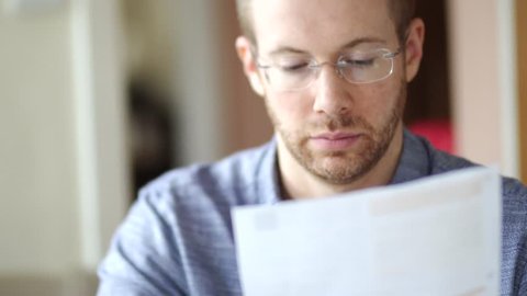 A man in debt is worried and stressed whilst looking through bill letters. Sad and anxious he holds his head in hands. White Caucasian young adult in 30's.