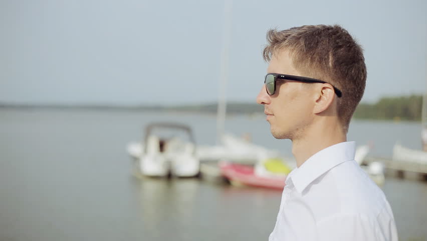A young man in sunglasses standing at the beach and looking far away