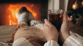 Closeup slow motion video of young woman warming at fireplace with cup of tea