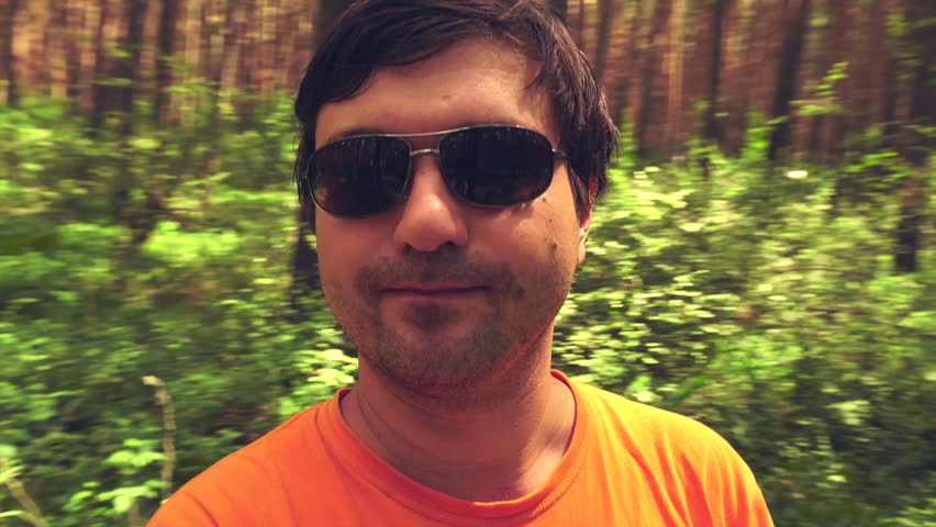 Portrait of a hipster with a short bristle in sunglasses who is spinning in the woods and smiling