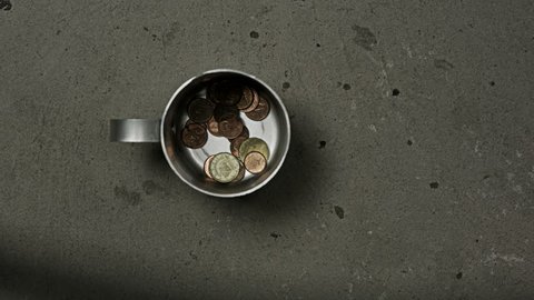 beggar's mug being filled with coins and dollar