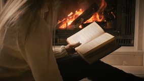 Slow motion video of woman sitting by the fireplace, reading book and drinking tea