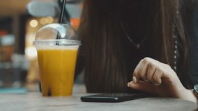 4k UHD slow motion video. Young woman browsing on smartphone in cafe on wooden table, drinking juce. Businesswoman typing text on mobile phone.
