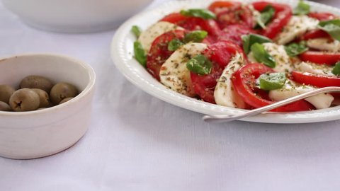 Caprese salad made of sliced fresh tomatoes, mozzarella cheese and basil  served on a white plate on a table.Traditional Italian food