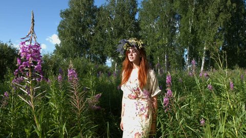A beautiful red-haired girl with a wreath on her head walks among the flowering willow-tea.
She stops at the flower and inhales his scent. Then she looks at the camera. Slow motion.