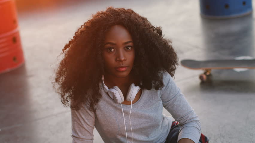 Young attractive african woman with headphone on the neck while she sitting on the roof with city background. Portrait shot.