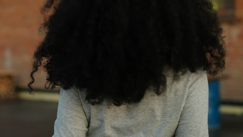 Close up back view of beatiful curly hair african woman in casual shirt walking on the roof.