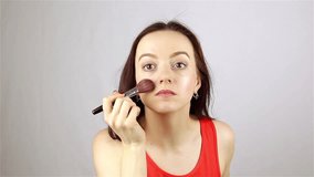 Girl applies makeup with a brush in front of a mirror on a gray background