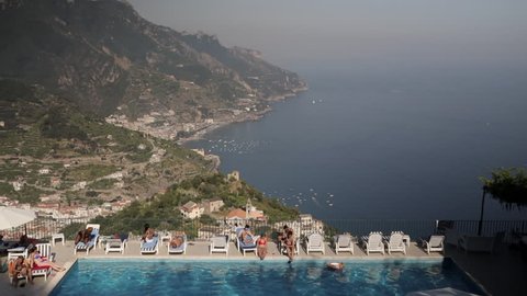 Ravello, Italy - July 25th, 2017: Stunning view of the Amalfi Coast with an outdoor swimming pool and beautiful tourists in a bikini in the foreground. Ravello, Italy. Luxury holidays.