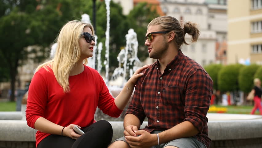 Girl comforting her sad boyfriend while sitting next to the fountain
