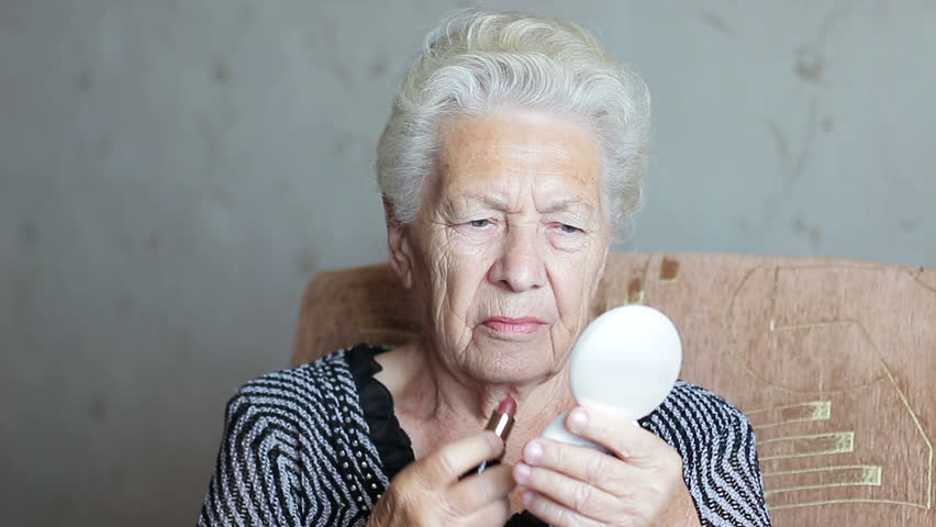 Old woman doing makeup. Lipstick