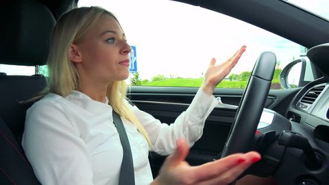 Young attractive blond woman drives a car (waits on the traffic lights) and scolds on other drivers 