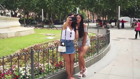 Two Chinese girls smiling taking selfie standing at Hispalis Font, in Seville, Spain