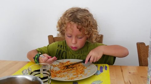 little blond boy eating pasta with tomato sauce