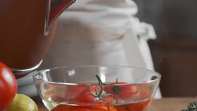 The cook blanchs tomatoes in a glass bowl with hot water, fresh vegetables, cooking vegetarian food, cooking food in the kitchen