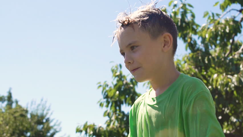 Slow motion of little cheerful boy standing in green summer backyard and being poured over with water by someone.