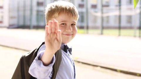  A smiling schoolboy waving good-bye and running to school.