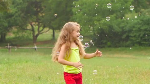 Smiling girl have fun playing catch soap bubbles in summer park. Slow motion