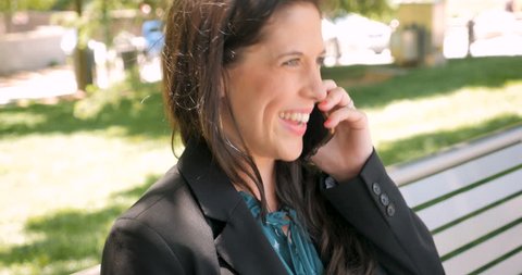 Successful happy businesswoman in her 30s talking on mobile phone on park bench in 4k hand held profile side view