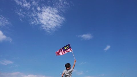 Unknown kid waving Malaysia Flag. Independence day and Merdeka Celebration. Blue sky and copy space