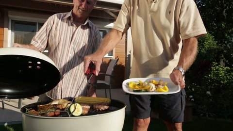 retirees cooking on kettle barbecue in garden
