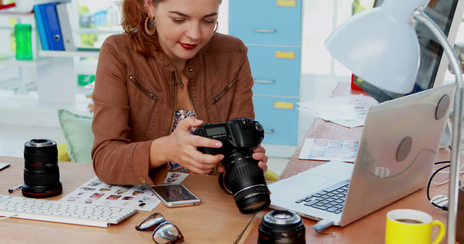 Female executive talking on mobile phone while looking photo on digital camera in office 4k