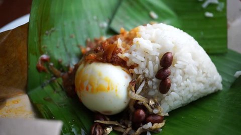 hands wrap a package of nasi lemak or Malaysia fragrant rice cooked in coconut milk and pandan leaf with banana leaf and paper on table