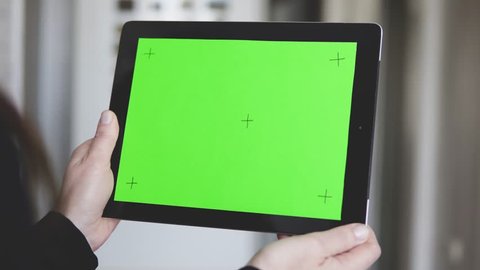 Woman wear in black sweater is holding a tablet pc with green screen and markers, making pick gestures on touchpad, defocused background, 4K