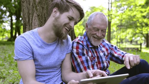 Young man and his senior father with tablet outdoors.