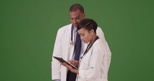 Two black expert medical professionals discuss a patient while on their tablet on green screen. On green screen to be keyed or composited.