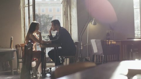 Romantic couple man and woman sitting at a cafe table. Loving couple man and woman drinking coffee in a cafe near an open balcony. View happy couple talking in a cafe during day