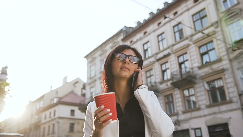Young business woman walking around the city,talking on the phone and drinking coffee slow motion