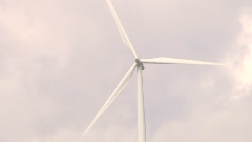 Wind turbine spinning along hillside in Washington on cloudy day, tilt up.