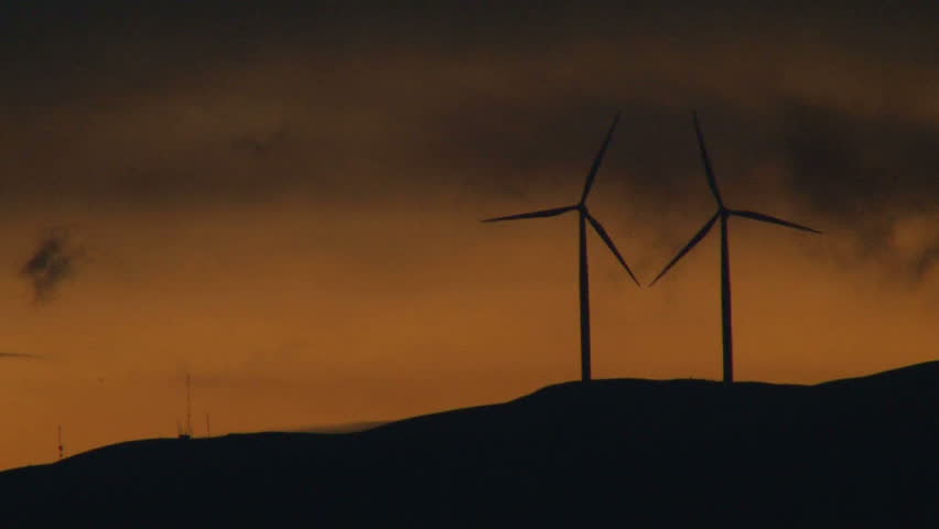 Two wind turbines spinning along hillside in Washington at sunset.