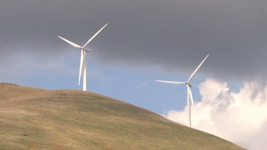 Two wind turbines spinning along hillside in Washington on cloudy day.