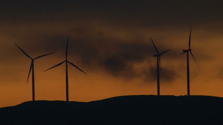 Four wind turbines spinning along hillside in Washington at sunset.