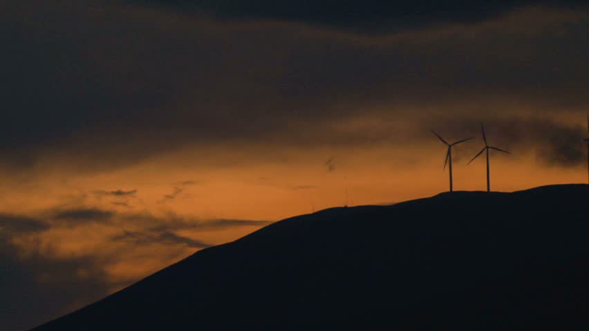 Two wind turbines spinning along hillside in Washington at sunset.