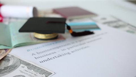 Graduation cap on a letter book, Business Goals, Concept of graduate education abroad in university, requires passport book and a lot foreign currency Dollars to bring success in famous institution.