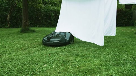 Robot lawn mower mows the lawn in a garden. Laundry on clothes line