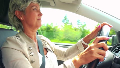 Middle aged woman drives a car, listens music and dances 