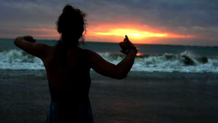 Silhouette of the woman standing on the seaside during sunset and feels free, steadycam shot
