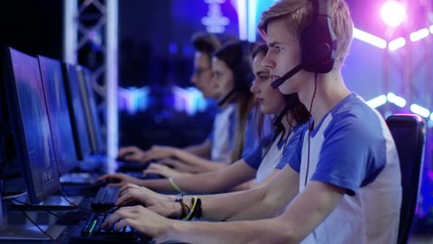 Team of Teenage Gamers Play in MMORPG Video Game on a eSport Tournament. Displays Show Beautiful Game, Players Speak into Headsets Microphones and Actively Play to Win. Shot on RED EPIC-W 8K Camera.